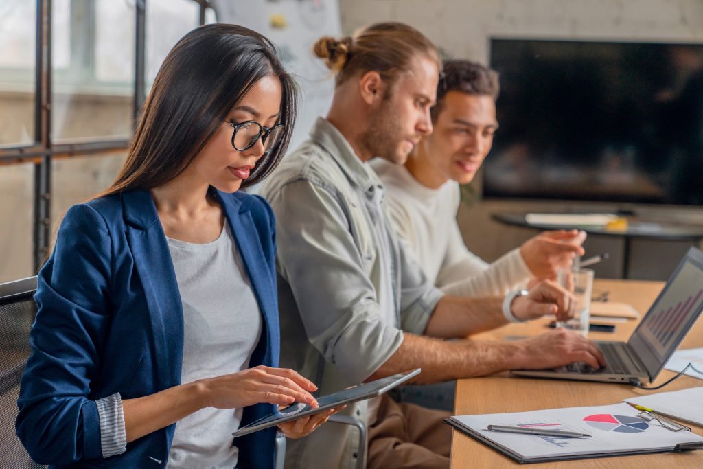 Asian female working on digital tablet. Young businessman in meeting with coworkers